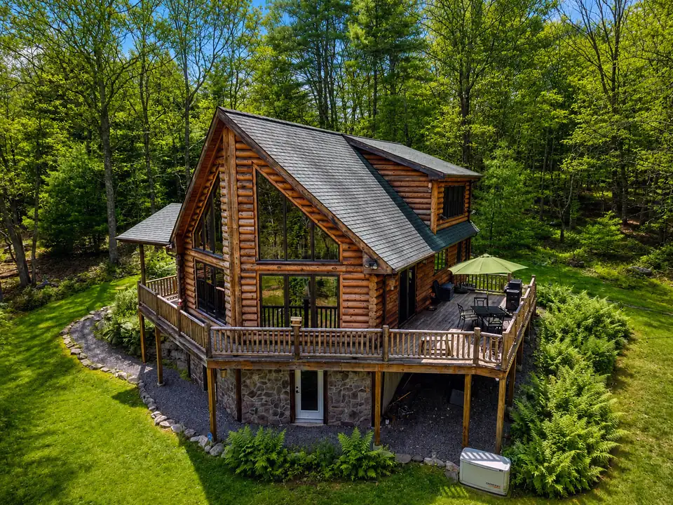 Aerial view of the Fernwood Lodge log cabin, deck, and lawn surrounded by green summer forest