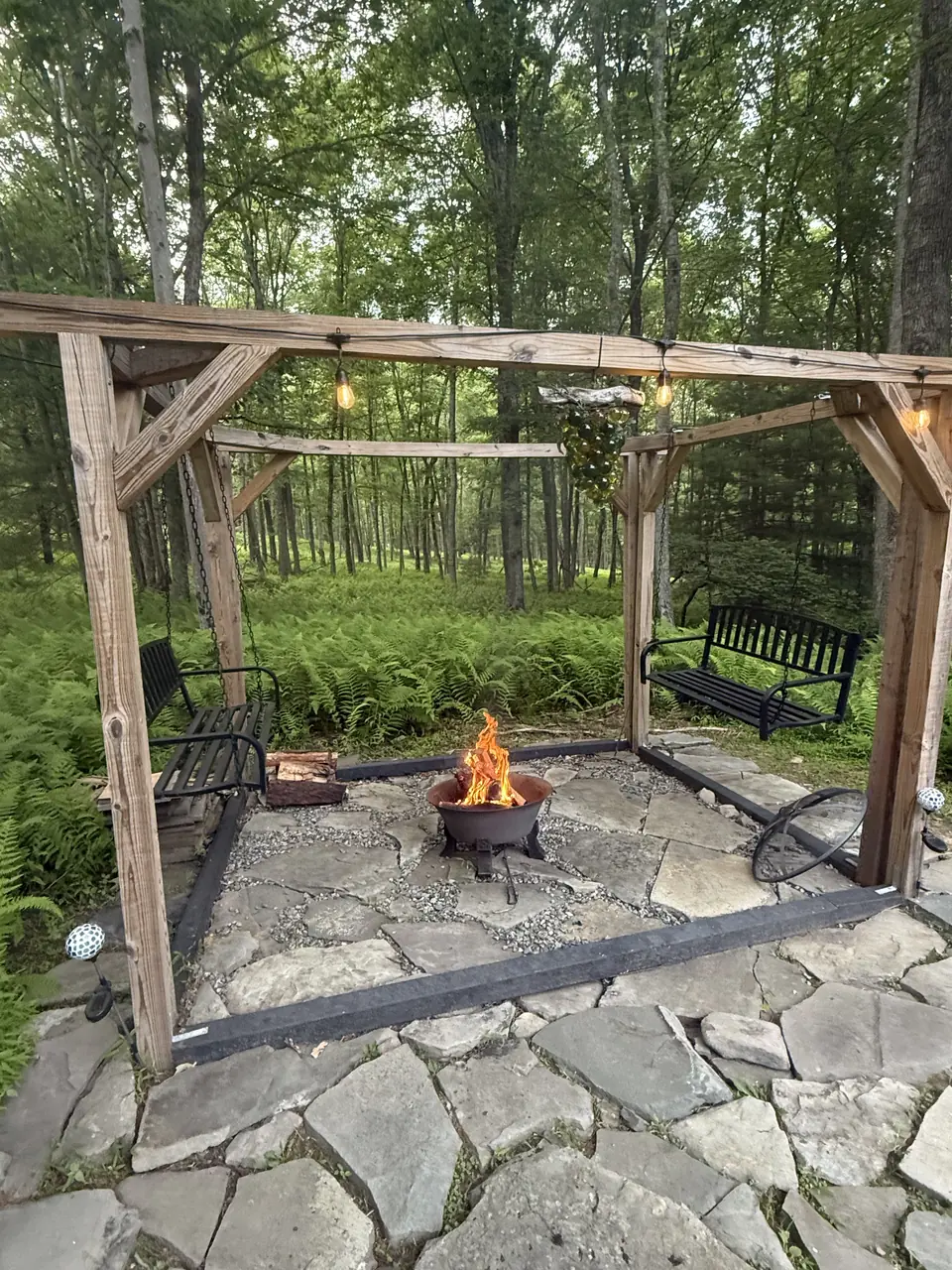 The fire pit burning under the timber pergola, surrounded by ferns