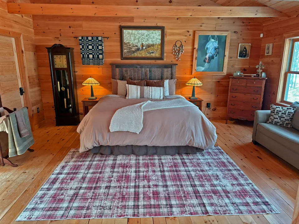 King bed in the primary suite with log walls, art, and a plaid rug